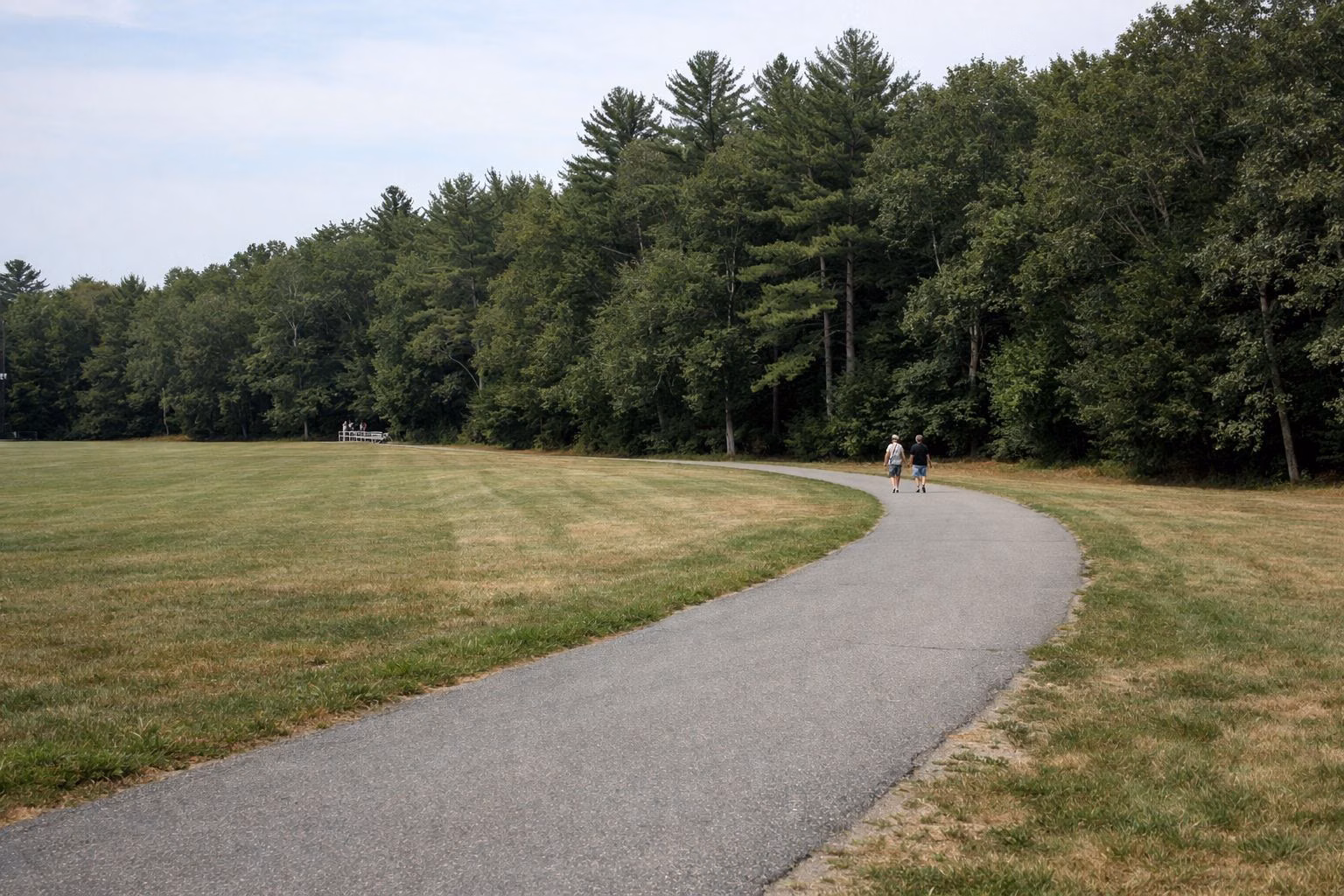 A paved walking path past a playing field in a town park