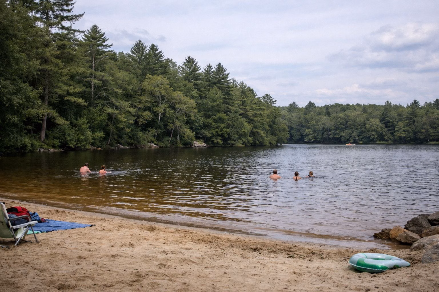 A small sandy town beach on a tree-lined pond